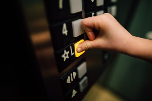 Hand pressing button on an elevator control panel.