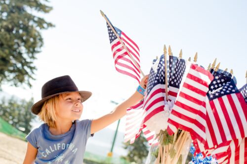 Young blonde girl in a hat waving an American flag at a fourth of July party