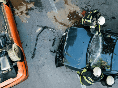 Three firefighters rescuing the inhabitants of a blue car after a traffic collision